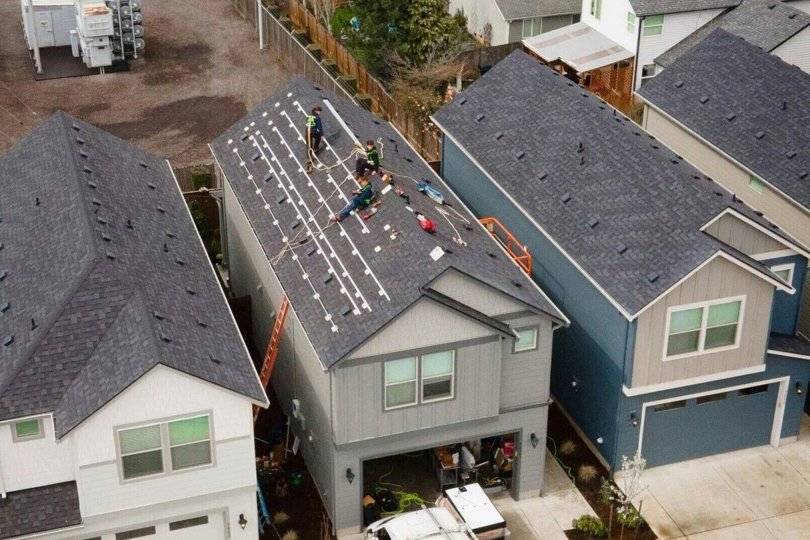 Drone shot of workers installing new roof panels in a suburban neighborhood.